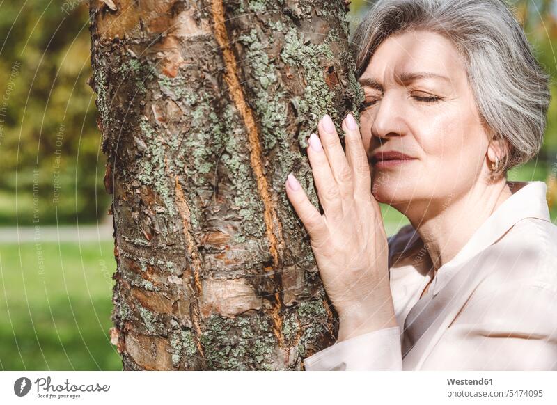 Woman with eyes closed embracing tree while standing at park color image colour image outdoors location shots outdoor shot outdoor shots day daylight shot