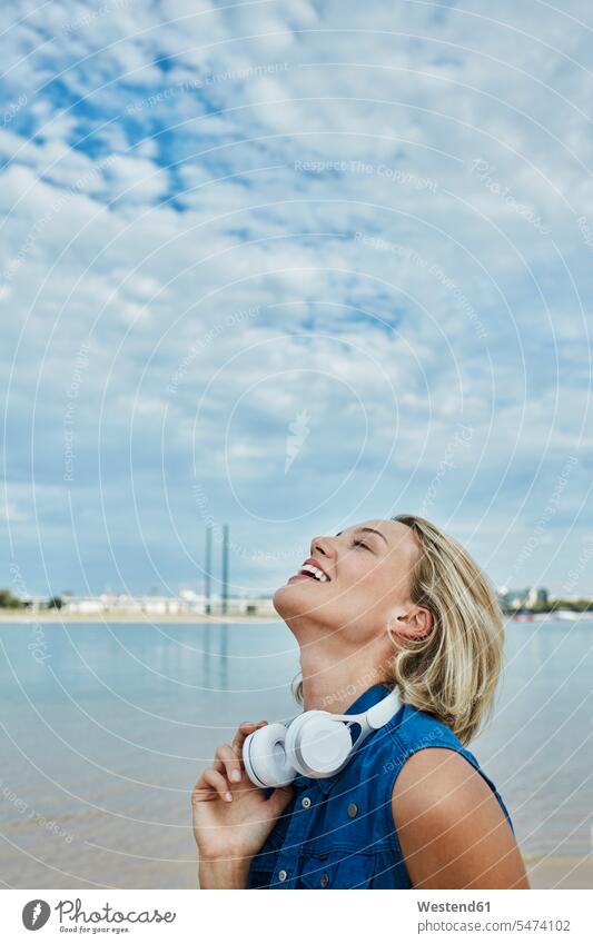 Germany, Duesseldorf, happy young woman with headphones at Rhine riverbank headset females women riverside River Rivers happiness Adults grown-ups grownups
