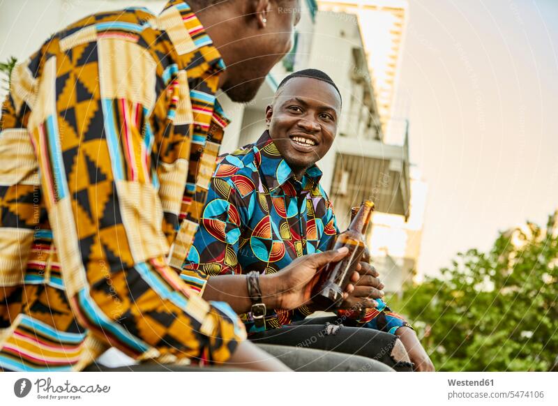 Friends sitting on roof terrace in the city drinking beer, Maputo, Mozambique friends mate Bottles Beer Bottles shirts smile Seated speak speaking talk relax