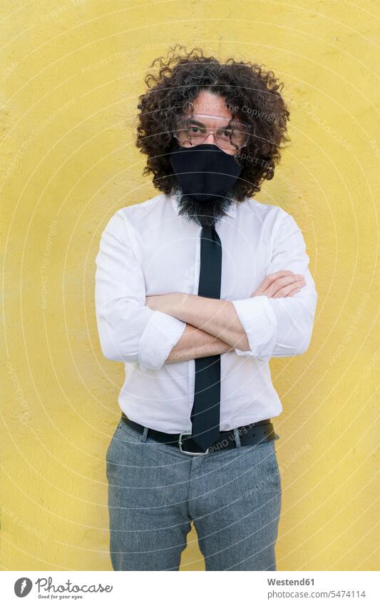 Businessman wearing face mask and eyeglasses standing with arms crossed against wall color image colour image outdoors location shots outdoor shot outdoor shots