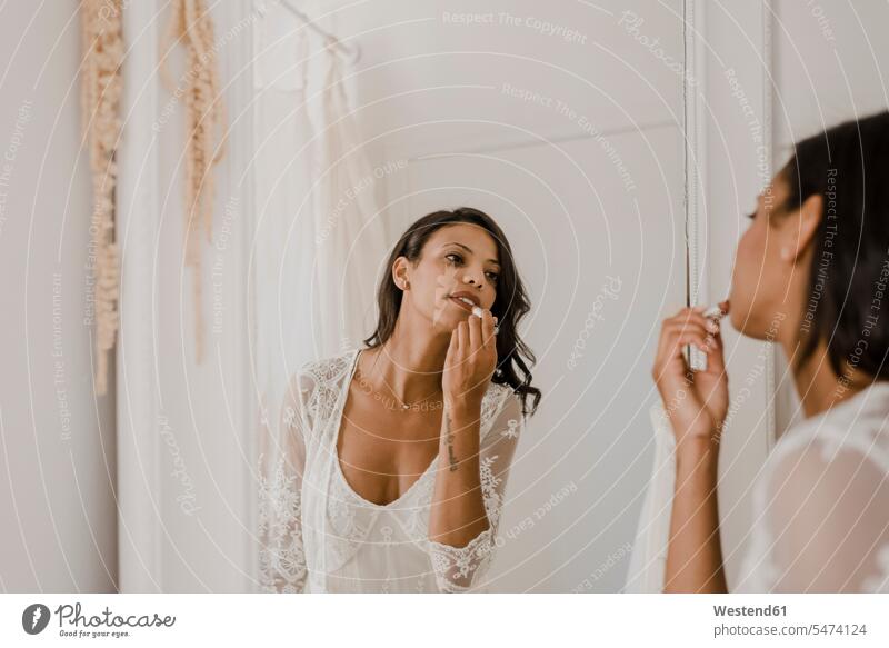 Young bride applying lipstick while looking in mirror at wedding dress shop color image colour image indoors indoor shot indoor shots interior interior view