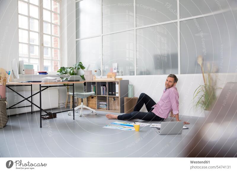Casual man with plans and laptop sitting on the floor in a loft office lofts floors offices office room office rooms casual Laptop Computers laptops notebook