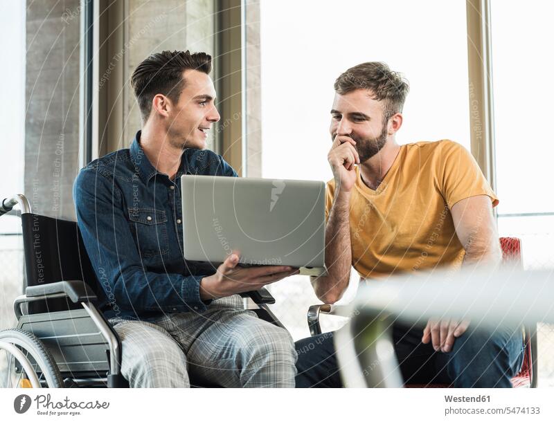 Young businessman in wheelchair showing laptop to colleague in office associate associates partner partners partnerships Occupation Work job jobs profession