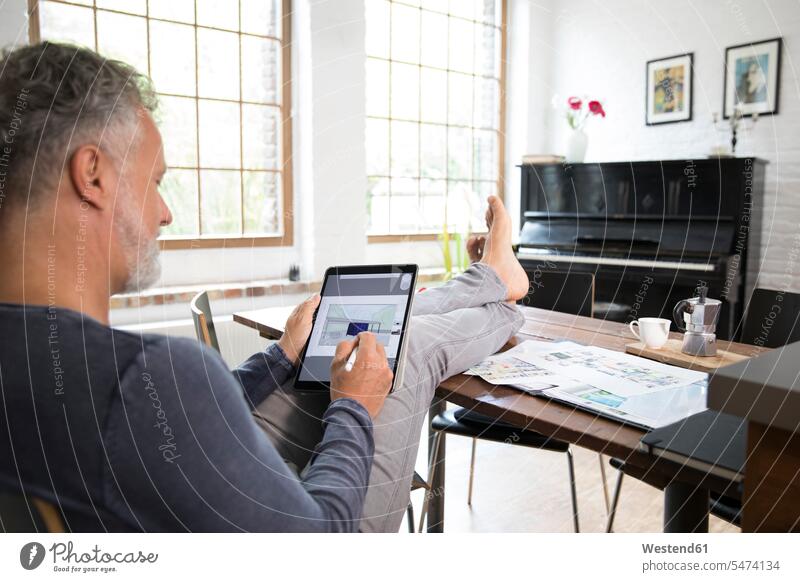 Mature man working from his home office with feet up, using tablet sitting Seated digitizer Tablet Computer Tablet PC Tablet Computers iPad Digital Tablet
