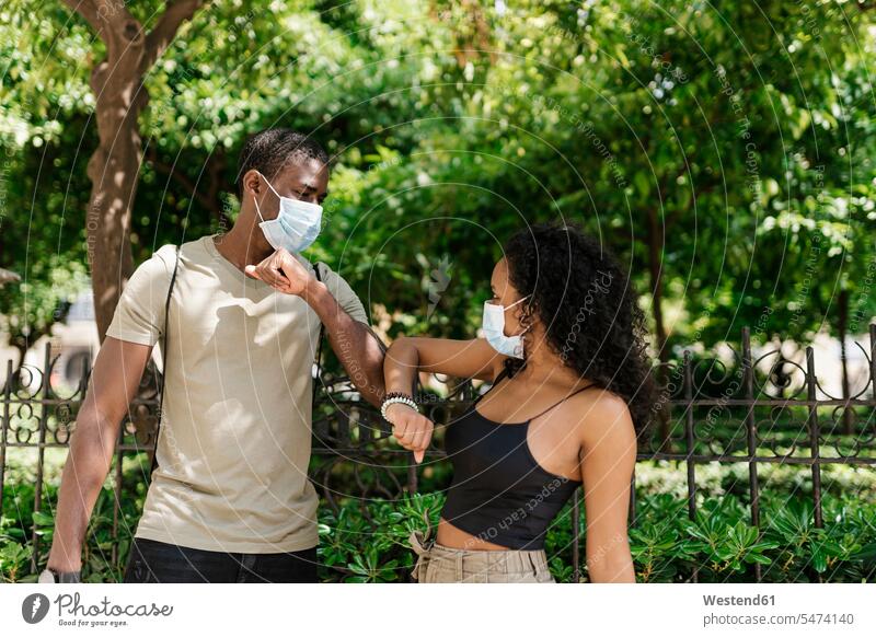 Man and woman wearing masks while greeting each other by touching elbows at park color image colour image outdoors location shots outdoor shot outdoor shots day
