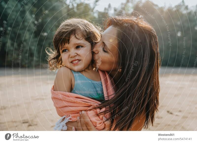 Mother kissing daughter at beach on sunny day color image colour image outdoors location shots outdoor shot outdoor shots daylight shot daylight shots day shots