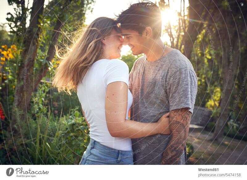 Happy young couple embracing and kissing in a park in summer touching parks Falling In Love young couples young twosome young twosomes embrace Embracement hug