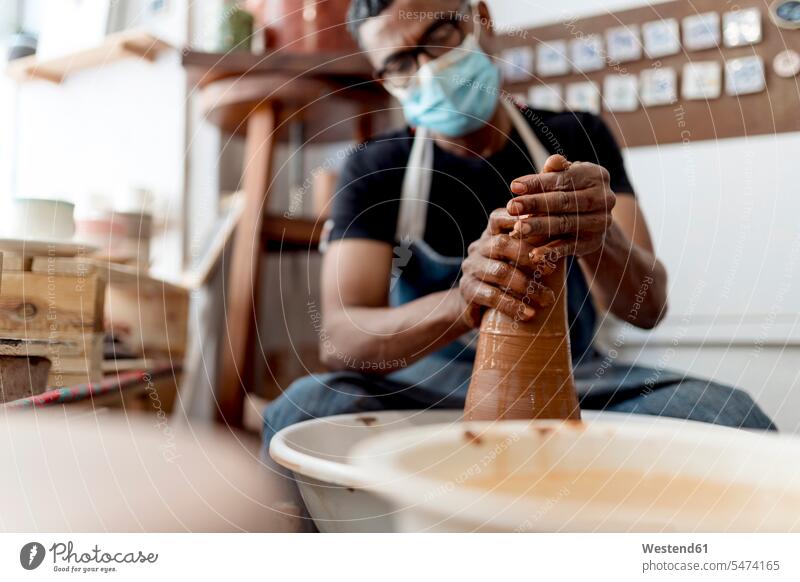 Male potter wearing mask molding shape to clay while sitting in workshop color image colour image Spain indoors indoor shot indoor shots interior interior view