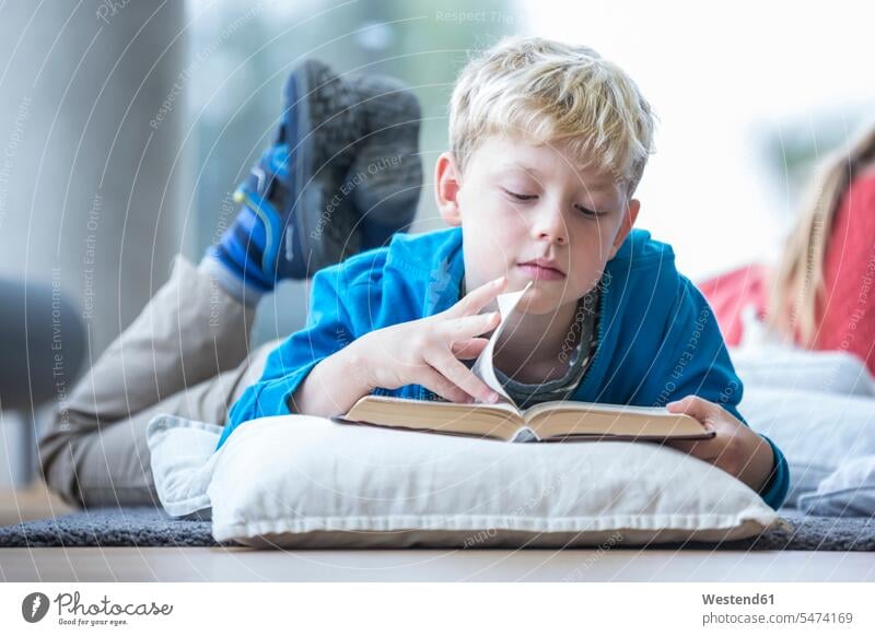 Schoolboy lying on the floor reading book in school break room floors schools Schoolboys laying down lie lying down books learning Intelligence intelligent