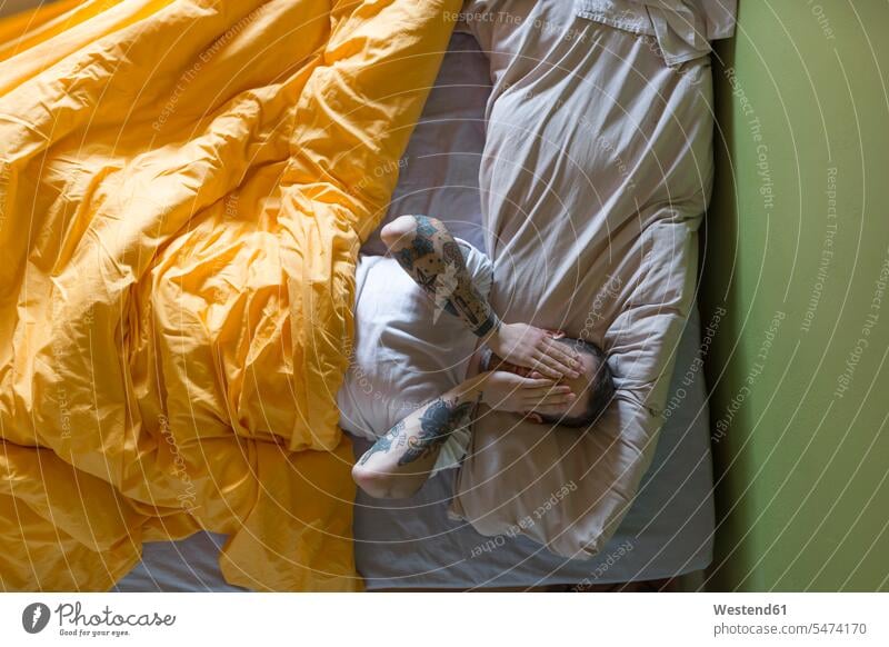 Tattooed man lying in bed, hands on eyes human human being human beings humans person persons caucasian appearance caucasian ethnicity european adult grown-up