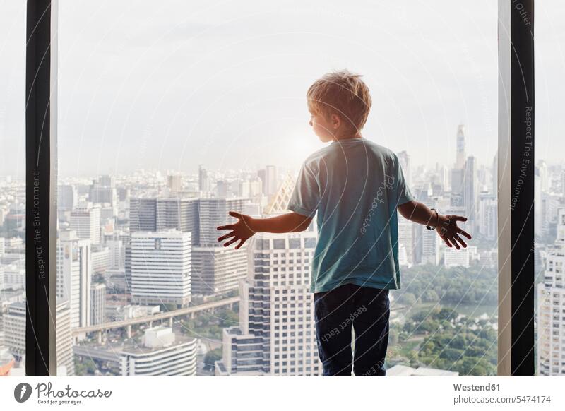 Thailand, Bangkok, boy looking through window at cityscape view seeing viewing boys males windows child children kid kids people persons human being humans