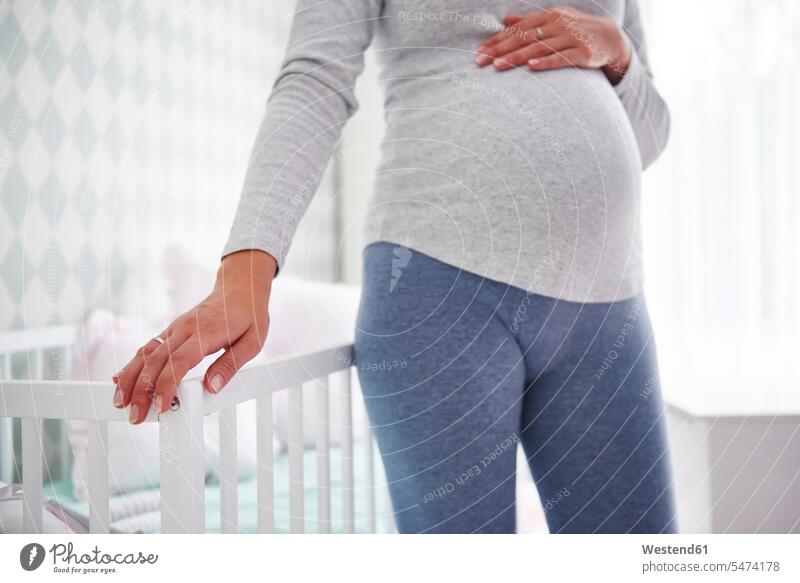 Pregnant woman standing on baby bed stroking petting portrait portraits baby cot baby crib baby room baby's room females women pregnant Pregnant Woman belly