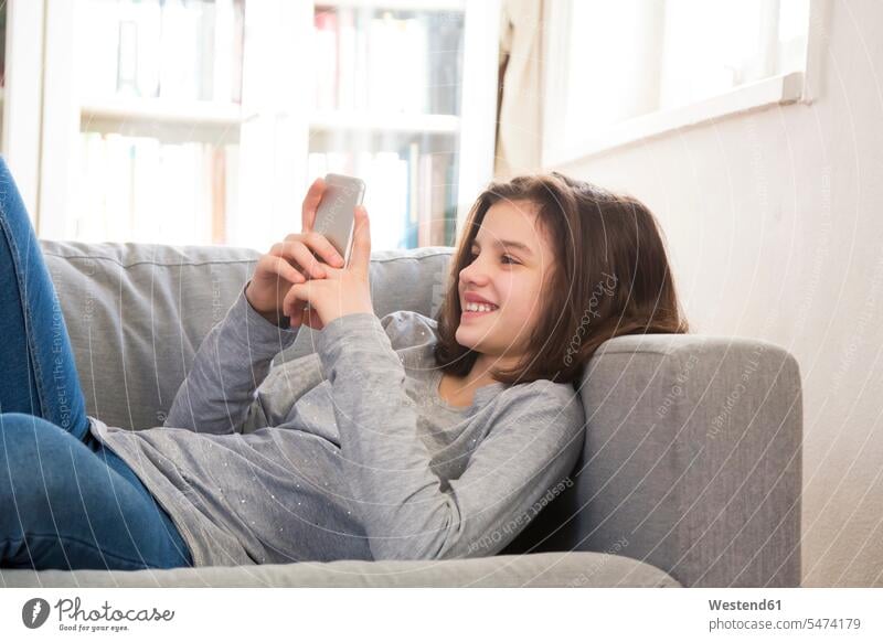 Smiling girl lying on couch at home using cell phone Smartphone iPhone Smartphones females girls smiling smile settee sofa sofas couches settees use laying down