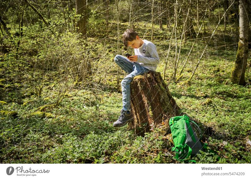 Full length of boy sitting on tree stump while using smart phone in Swabian Jura forest during hiking color image colour image outdoors location shots