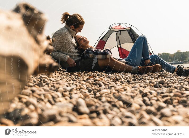 Happy young couple relaxing at a tent at the riverside happiness happy tents riverbank twosomes partnership couples relaxed relaxation water's edge waterside
