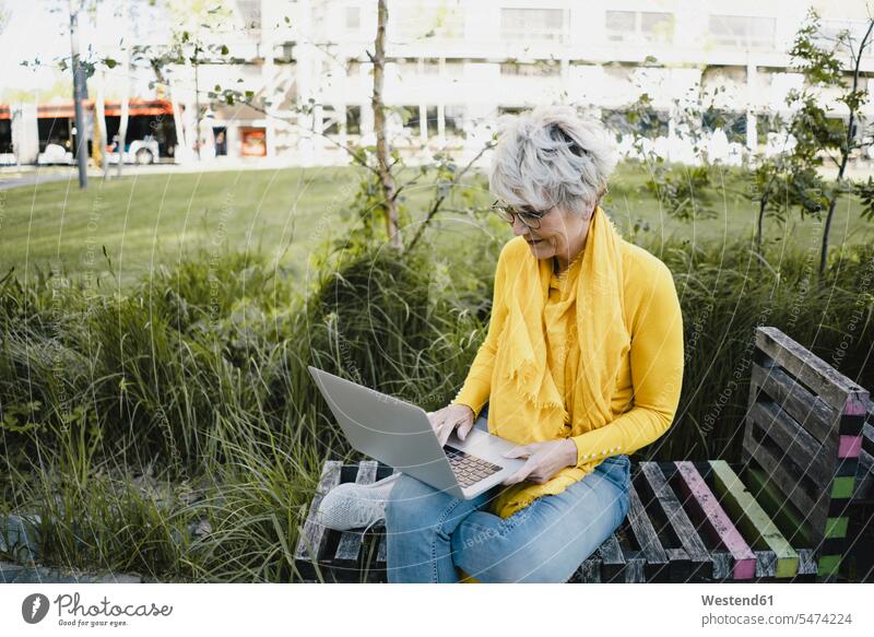 Mature woman sitting on bench outdoors using laptop human human being human beings humans person persons celibate celibates singles solitary people