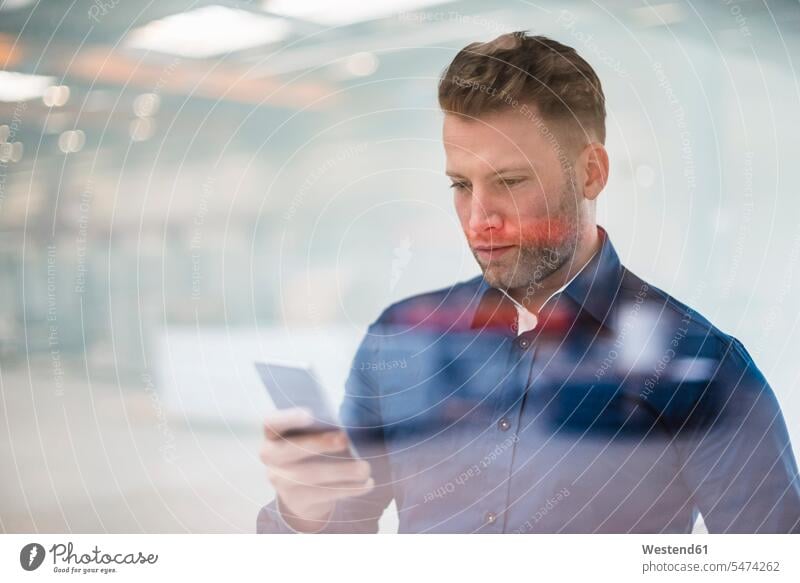 Businessman looking on cell phone behind glass pane eyeing glass panes Business man Businessmen Business men mobile phone mobiles mobile phones Cellphone
