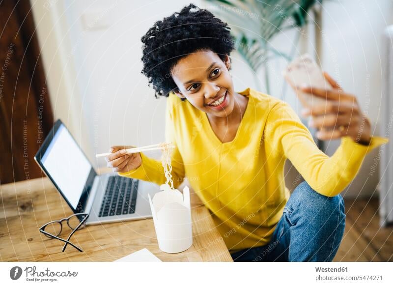 Smiling young woman sitting at table with laptop and noodles, taking a selfie Table Tables young women Selfie Selfies Noodle Noodles Seated Laptop Computers