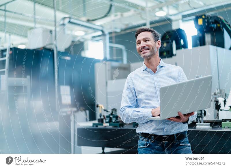 Happy mature businessman holding laptop while working in industry indoors indoor shot indoor shots interior interior view Interiors Germany front view frontal