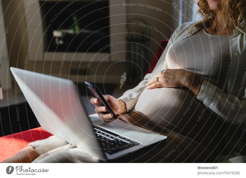 Pregnant businesswoman using mobile phone and laptop on sofa at home color image colour image indoors indoor shot indoor shots interior interior view Interiors