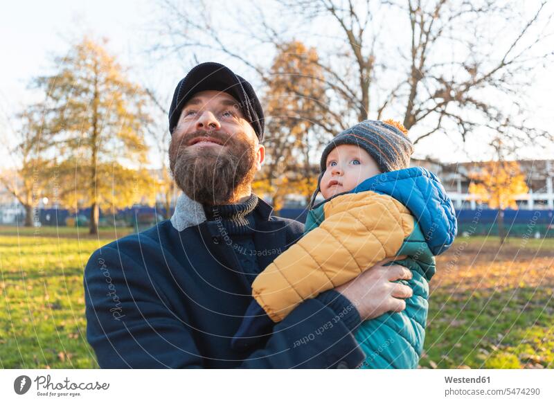 Happy man with his baby son at park coat coats jackets caps hat hats hold smile delight enjoyment Pleasant pleasure Secure indulgence indulging savoring happy