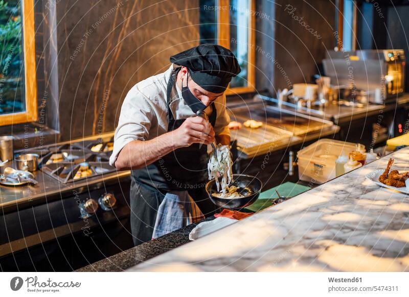 Chef wearing protective face mask preparing a dish in frying pan in restaurant kitchen human human being human beings humans person persons 1 one person only