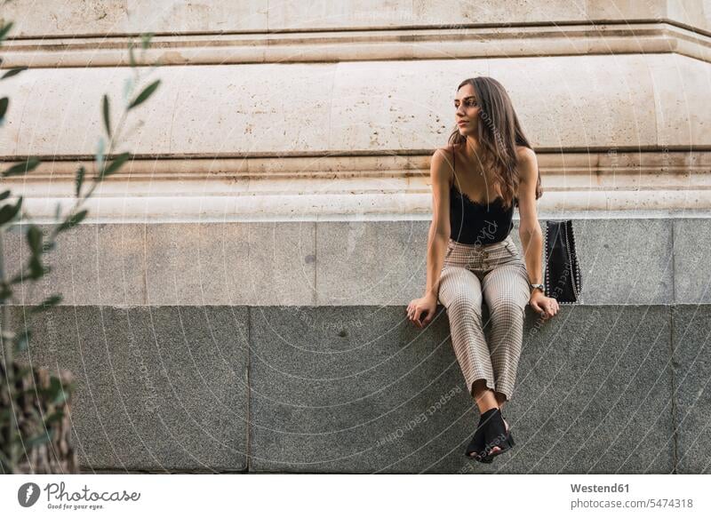 Young woman sitting on a wall waiting Seated females women walls Adults grown-ups grownups adult people persons human being humans human beings caucasian