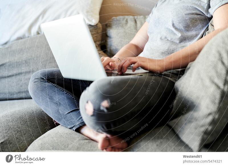 Low section of freelancer using laptop while sitting on sofa at home color image colour image Germany using a laptop Using Laptops Seated couch couches sofas