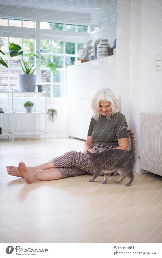 Retired woman sitting on floor while looking at cat in apartment color image colour image Denmark Scandinavia Scandinavian Peninsula indoors indoor shot
