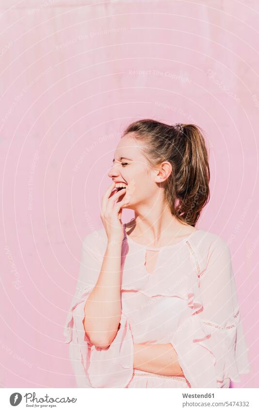 Laughing young woman in front of pink wall walls females women Rosy laughing Laughter Adults grown-ups grownups adult people persons human being humans