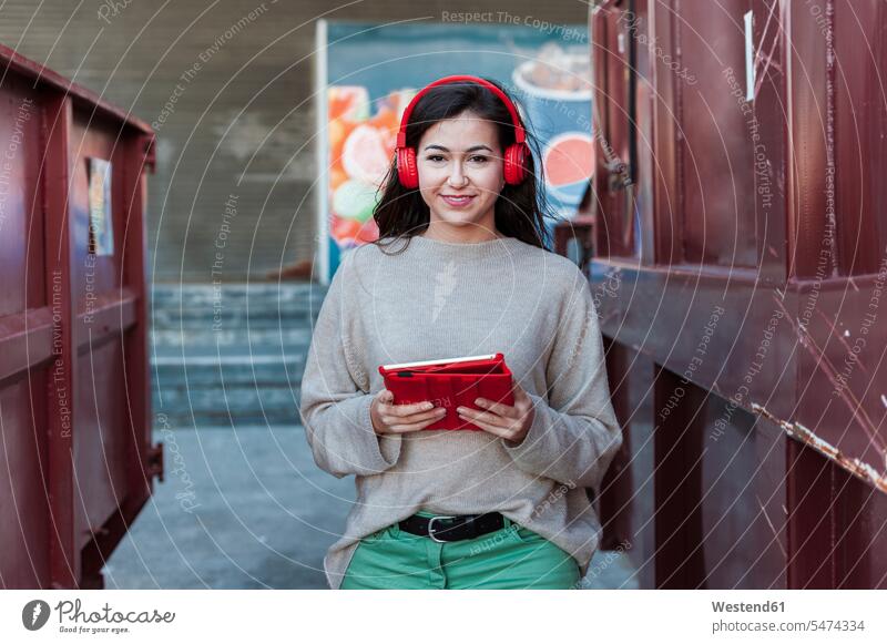 Smiling beautiful woman listening music on headphones while holding digital tablet color image colour image outdoors location shots outdoor shot outdoor shots