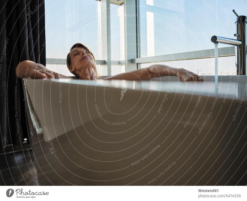Relaxed senior woman taking bath in bathtub against window at luxury hotel room color image colour image indoors indoor shot indoor shots interior interior view