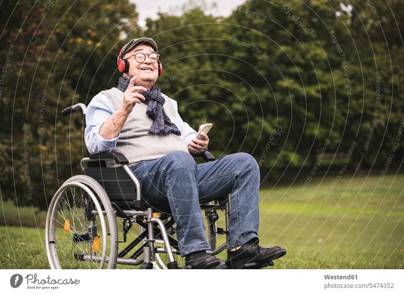 Portrait of happy senior man sitting in wheelchair listening music with smartphone and headphones human human being human beings humans person persons