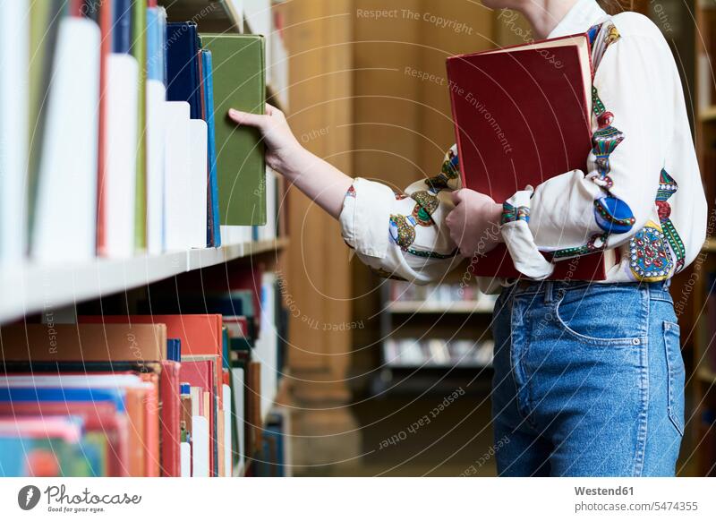 Female student with a book in a public library, choosing one taking take woman females women reading female students books Adults grown-ups grownups adult