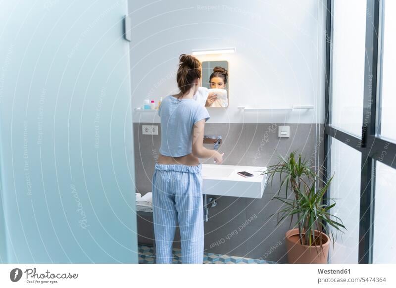 Rear view of young woman brushing teeth in bath room basin basins towels tooth-brush tooth-brushes toothbrushes mirrors telecommunication phones telephone