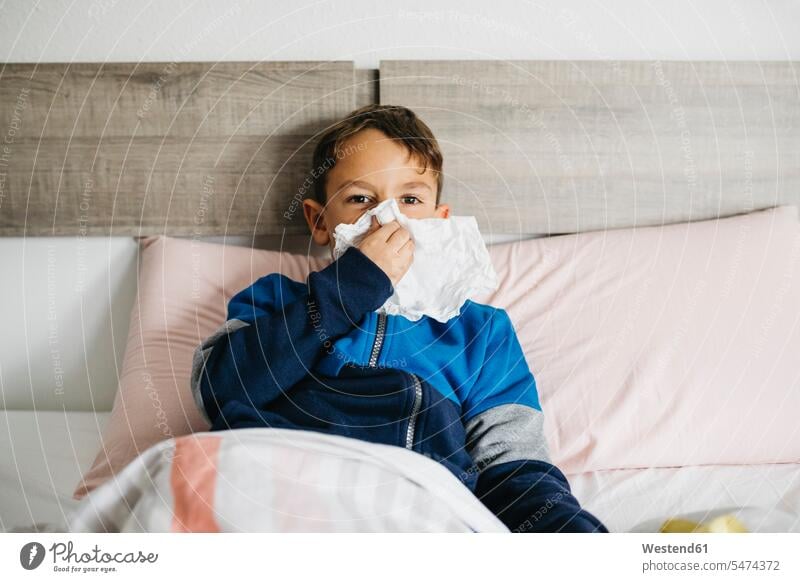 Portrait of sick boy lying in bed blowing nose handkerchiefs at home front front views frontal Frontal View head on head-on View From Front indoor indoor shot