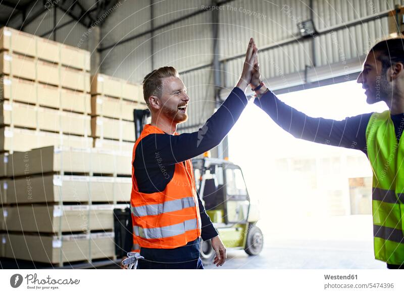 Happy colleagues in protective workwear high fiving in factory High Five Hi-Five high-fiving High-Five Protective Workwear Protective Work Wear worker