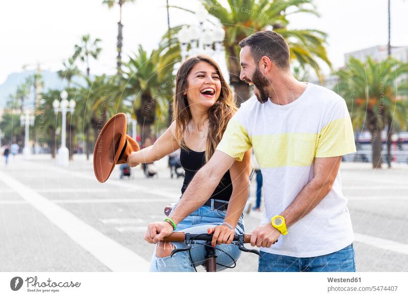 Spain, Barcelona, couple having fun and sharing a ride on a bike together on seaside promenade Fun funny promenades twosomes partnership couples bicycle bikes