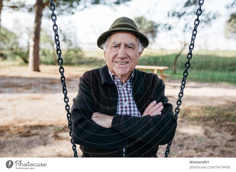 Old man sitting on swing in park, with arms crossed hats playground swing Swing - Play Equipment swing set swings swingset smile delight enjoyment Pleasant