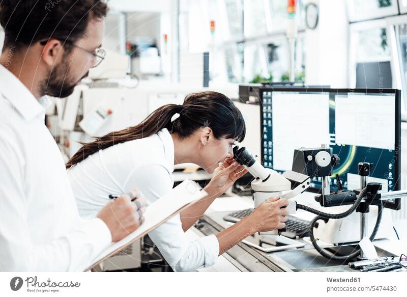 Female business professional looking through microscope while standing by male colleague at laboratory color image colour image Germany indoors indoor shot