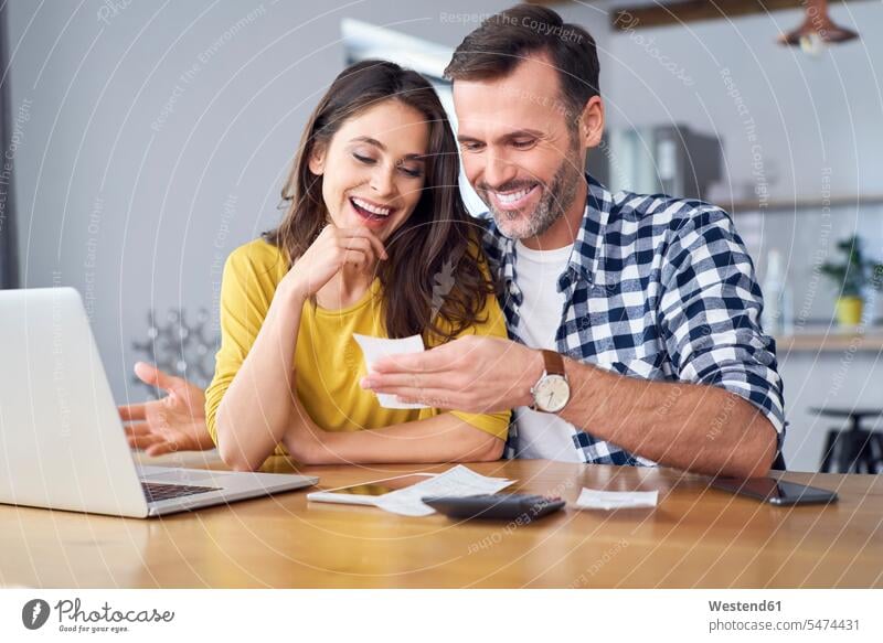 Couple sitting at dining table, using laptop, checking bills using a laptop Using Laptops Seated Table Tables home at home paying couple twosomes partnership