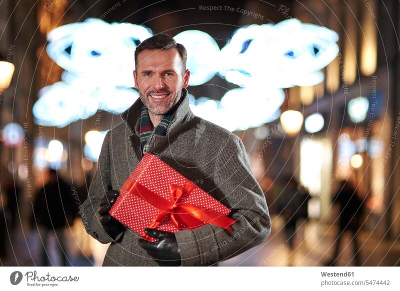 Portrait of smiling man with Christmas present looking at pedestrian area in the evening pedestrian zone smile Christmas presents men males portrait portraits