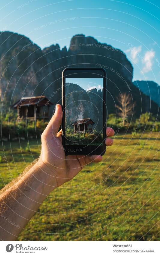 Laos, hand holding smartphone, Display with wooden hut and mountains Contemplation reflection Contemplating contemplate thinking huts Smartphone iPhone