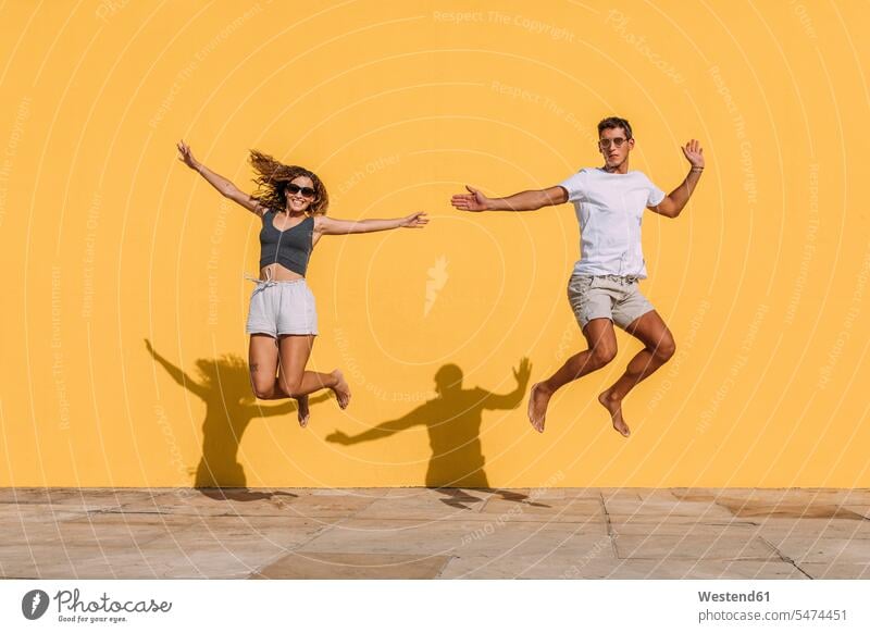 Young couple jumping in front of a yellow wall T- Shirt t-shirts tee-shirt Eye Glasses Eyeglasses specs spectacles Pair Of Sunglasses sun glasses jumps Leaping
