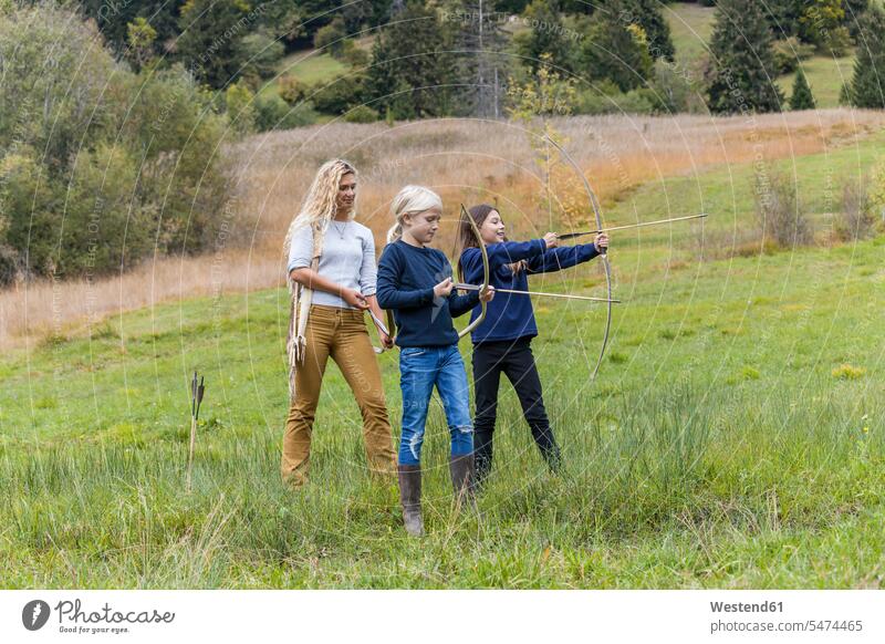 Young archeress teaching two girls aiming with bows females woman women educating educate archers female archer Archery Bows child children kid kids people