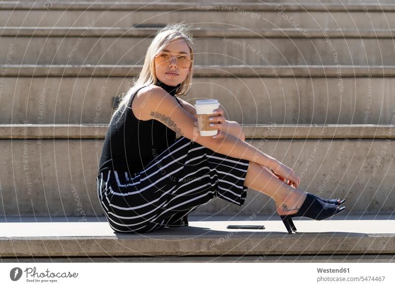 Bortrait of blond young woman with coffee to go sitting on stairs outdoors Spain Coffee to Go takeaway coffee beautiful Smartphone iPhone Smartphones