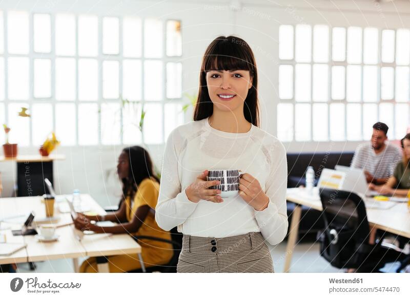 Portrait of smiling young woman in office with colleagues in background females women Coffee portrait portraits offices office room office rooms smile Adults
