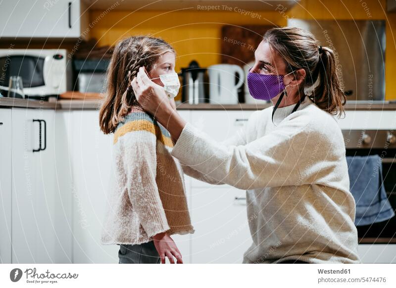 Mother adjusting daughter face mask while sitting at home color image colour image indoors indoor shot indoor shots interior interior view Interiors