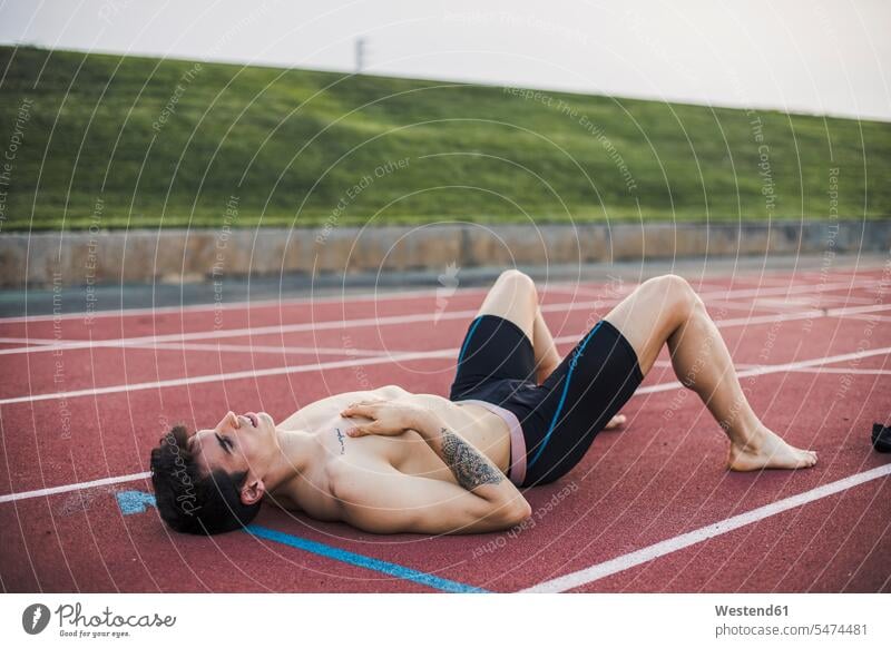 Athlete lying resting on a tartan track after finishing a race Southern European Ethnicity laying down lie lying down exercising exercise training practising