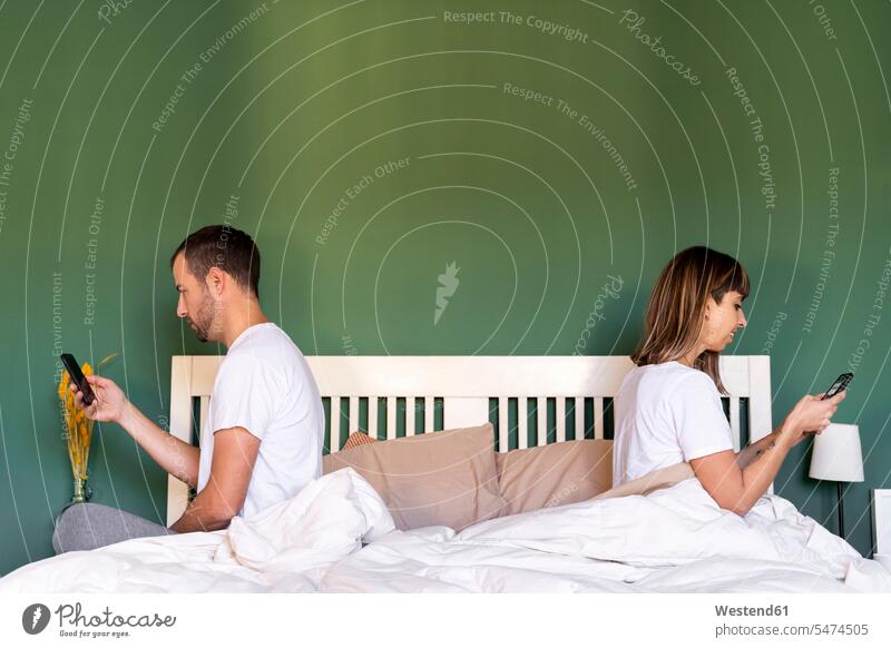 Mid adult couple using mobile phone while sitting on bed at home color image colour image indoors indoor shot indoor shots interior interior view Interiors